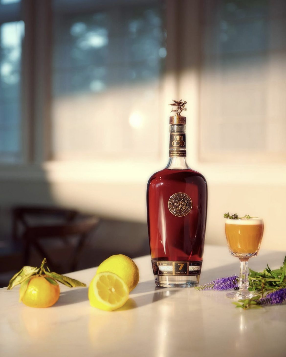 A bottle of Saint Cloud with a cocktail and cut citrus