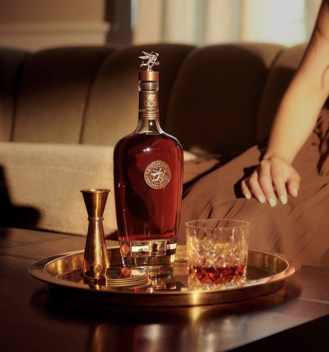 A bottle of Saint Cloud on a brass tray beside a cocktail and a rocks glass